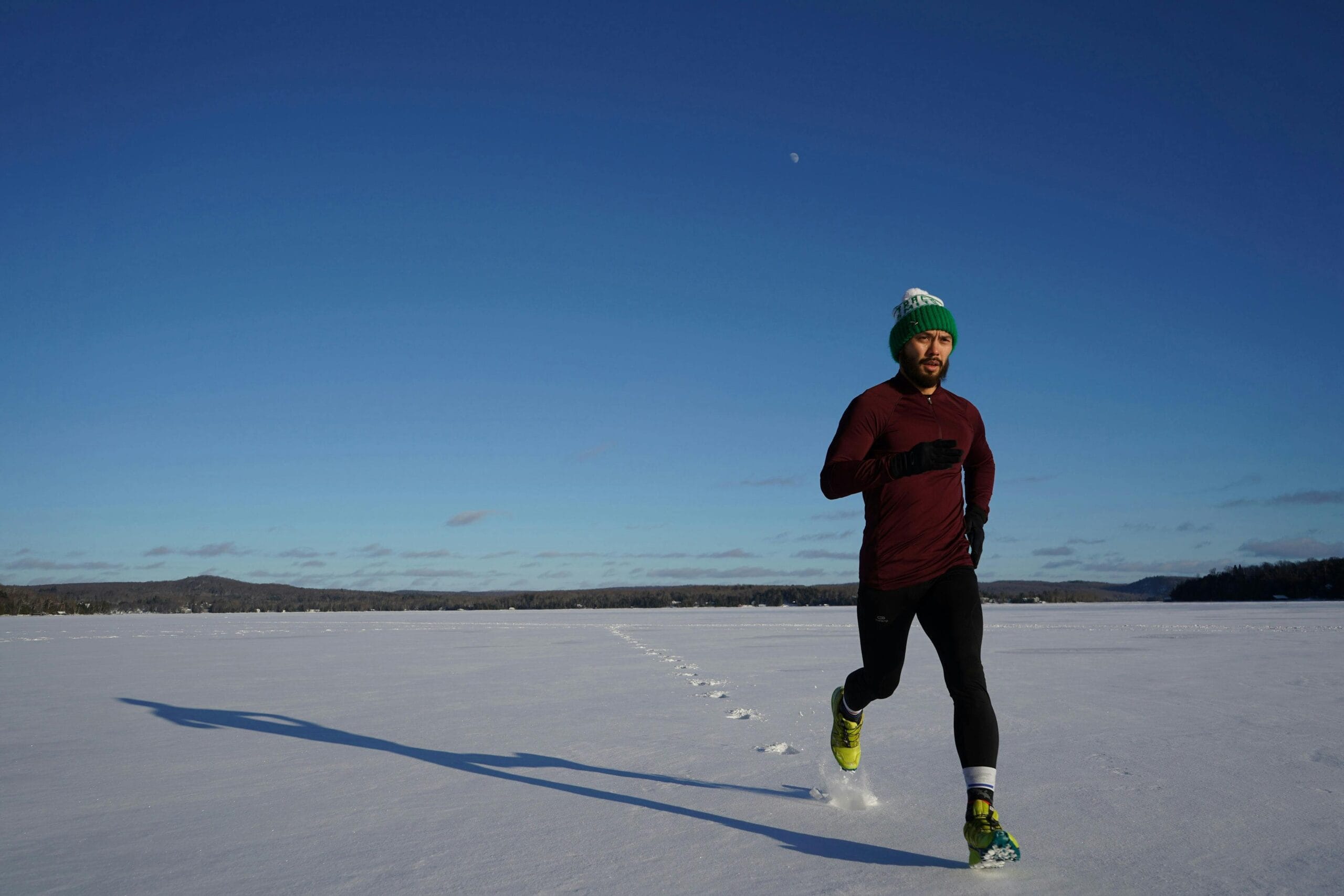 Man running on a snowy field in winter under clear blue skies.