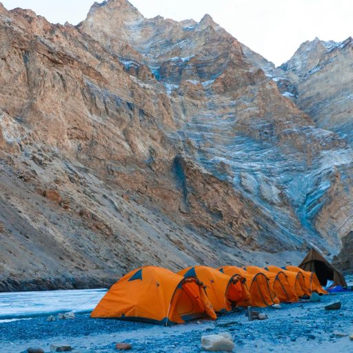 Row of orange tents on a rocky terrain against majestic mountains in Ladakh at daylight.